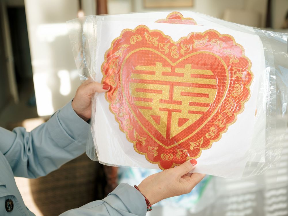 Someone holding traditional Chinese red heart-shaped paper cutouts with double happiness symbols in their hand.