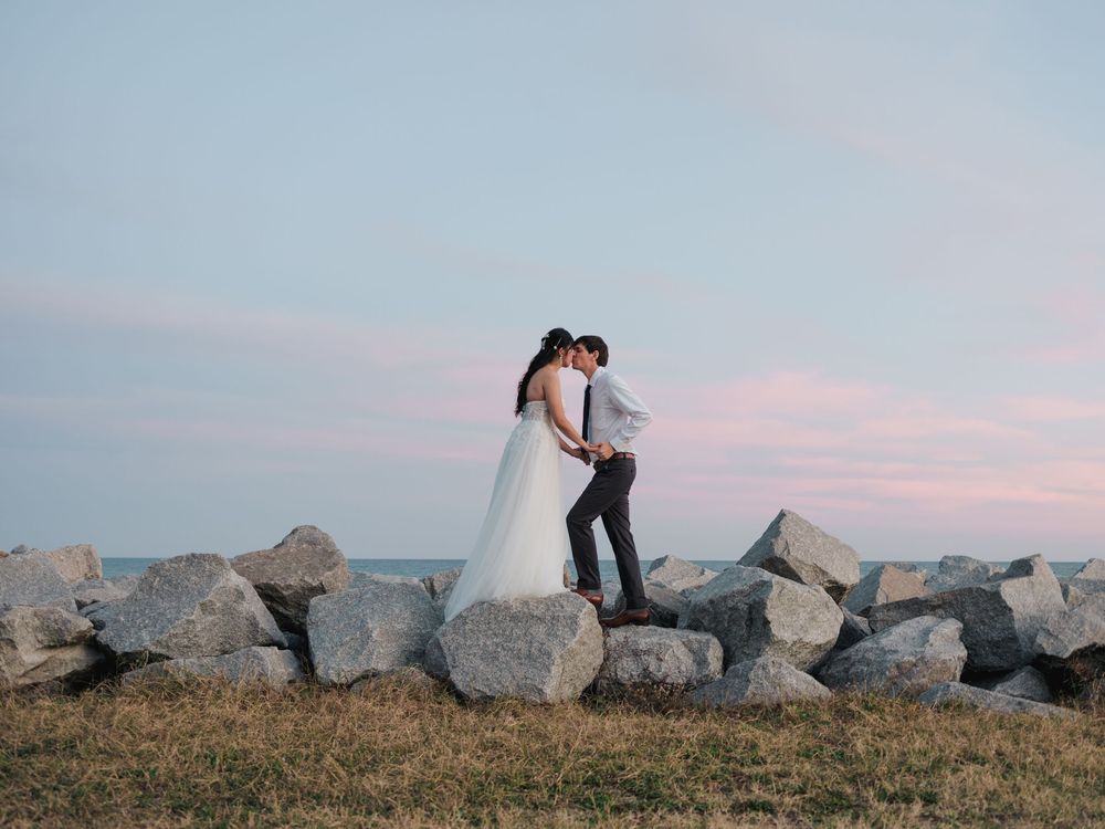 Couple in wedding attire share romantic moments against a rustic rocky backdrop during sunset.