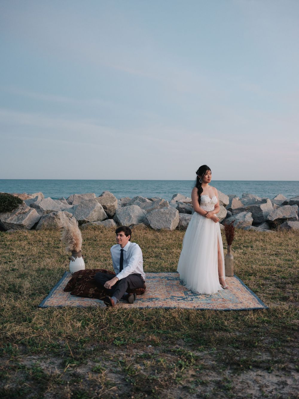 A romantic wedding photoshoot on a rocky beach with ocean views at sunset.