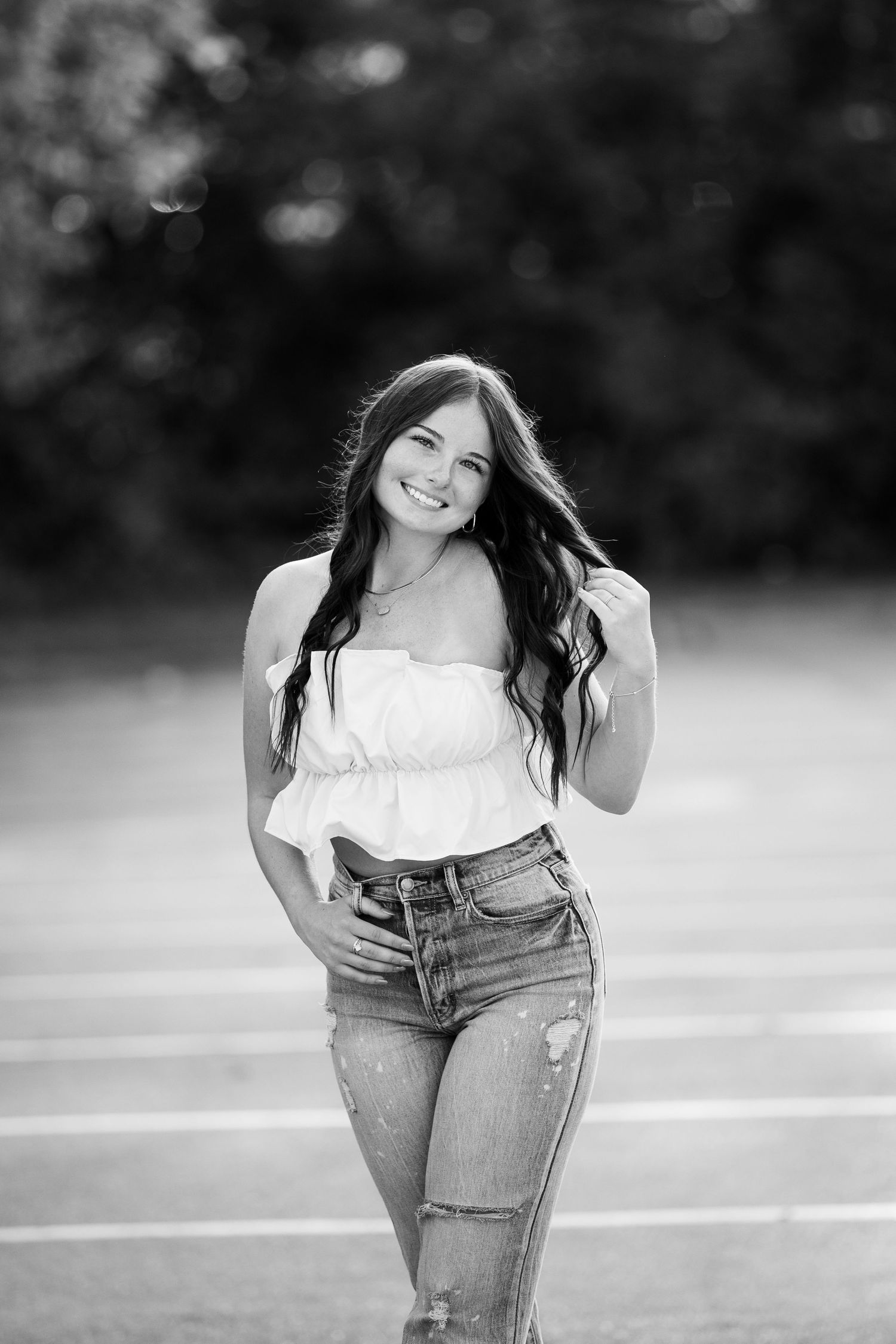 Black and white portrait photo of someone in a casual outfit of jeans and white top posing outdoors.