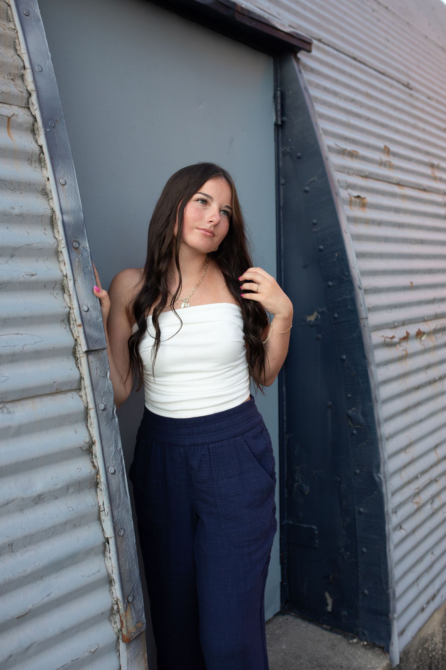A fashion model in a white top and navy pants poses against an industrial metal wall in a series of artistic shots.