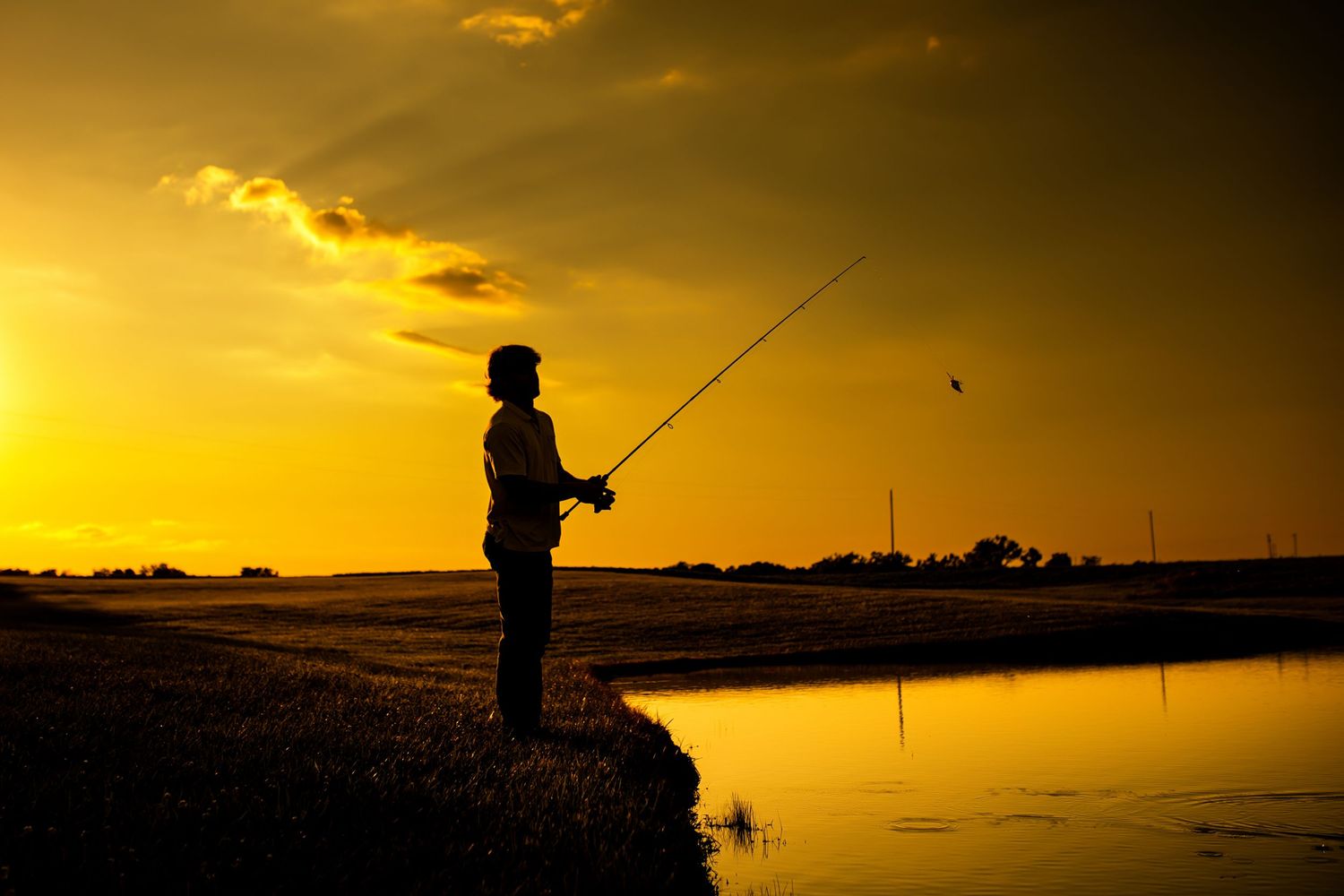 Silhouettes of people fishing on a pier against a vibrant golden sunset sky over the water.
