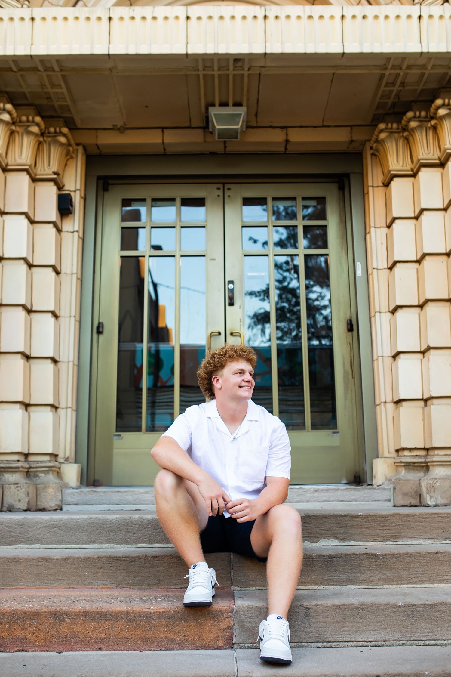 Someone wearing white sits alone on stone steps outside a building with pillars.