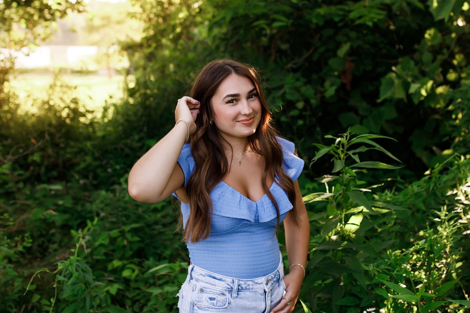 Woman in blue top poses playfully in lush garden setting during golden hour sunlight.
