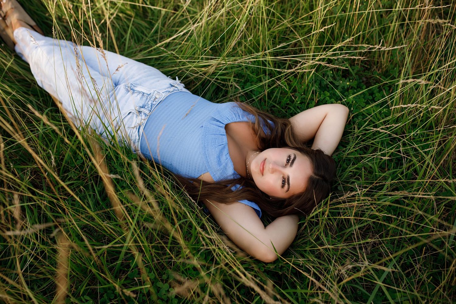 Person lying down in tall grass wearing a simple outfit against a natural outdoor backdrop.