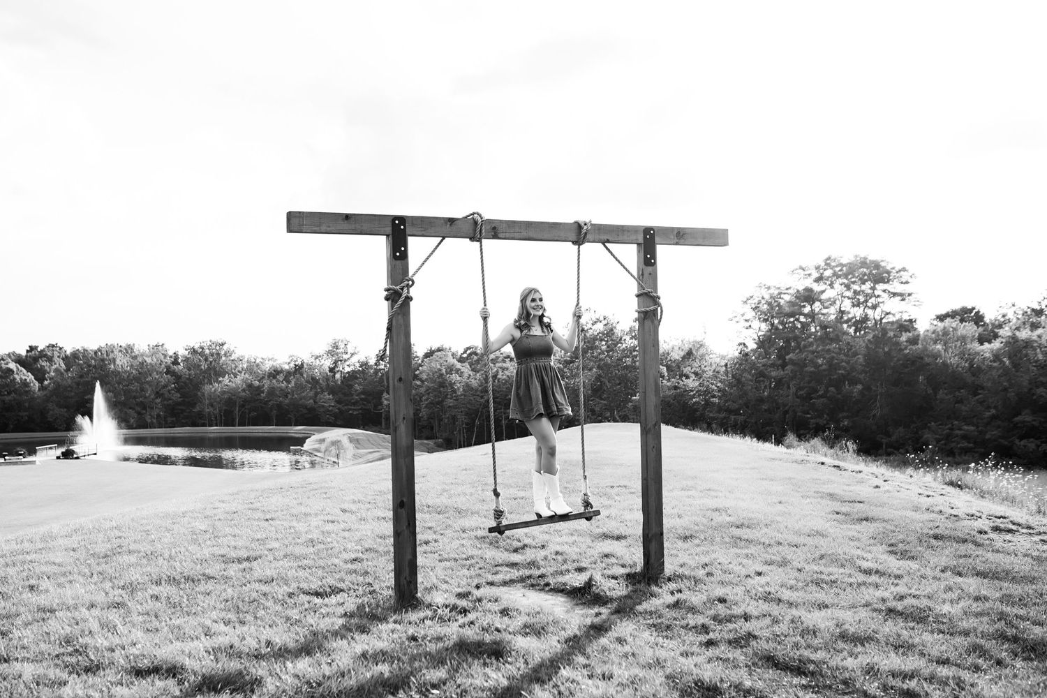 A rustic wooden swing frame sits empty on a grassy hilltop against a bright cloudy sky.