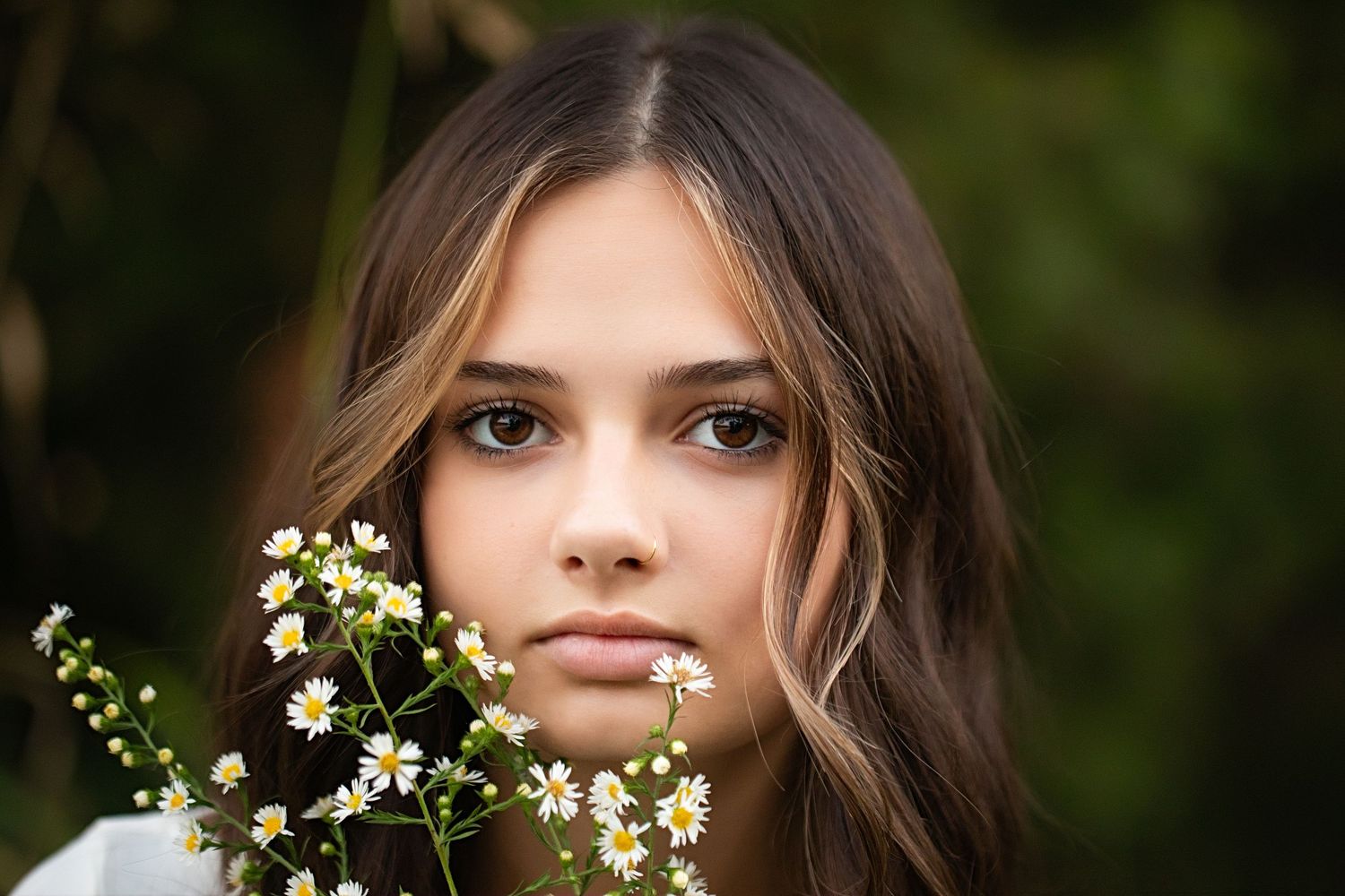 Close-up portrait with white wildflowers in soft natural lighting against a blurred green background.