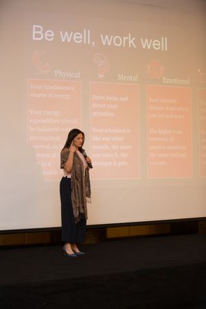 Speaker presenting wellness concepts with 'Be well, work well' slide in conference room.