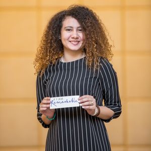 Person in striped shirt holding up a handwritten sign against orange background.