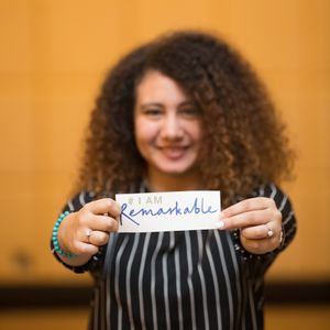 Woman with curly hair displaying a handwritten note while wearing black and white striped top.