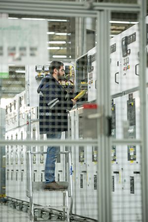 Industrial worker checking electrical control panels in manufacturing facility.
