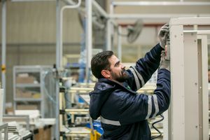 Worker in navy jacket performing maintenance on industrial equipment.