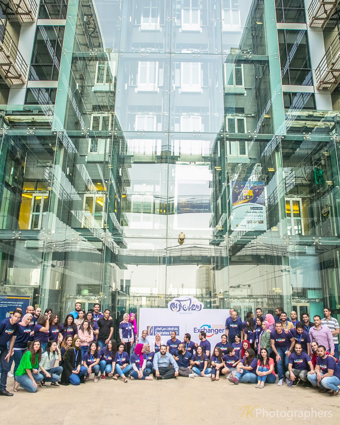 Large group photo in modern glass atrium building with high ceilings.