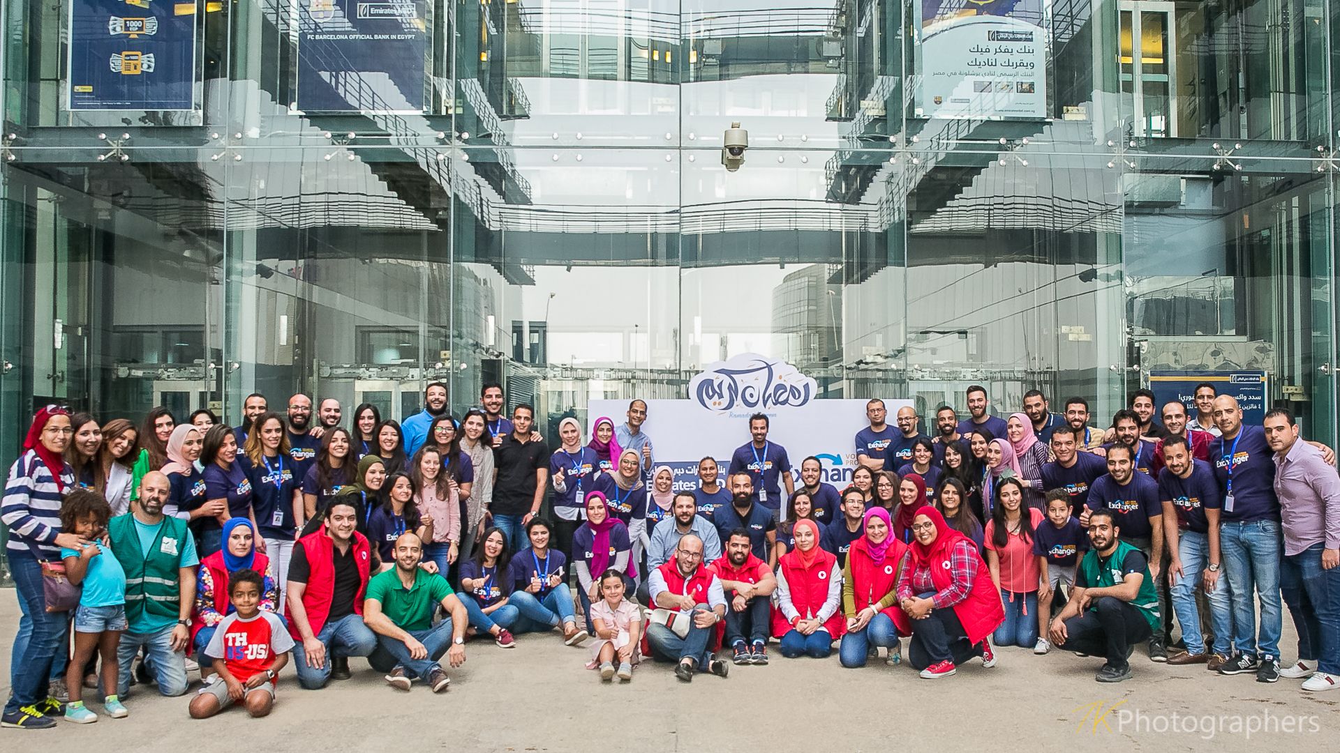 Diverse crowd gathered for group photo in modern glass-walled architectural space.