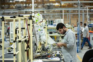 Factory worker operating technical equipment at an industrial assembly station.