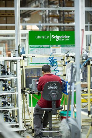 Worker operating equipment at a Schneider Electric manufacturing station.