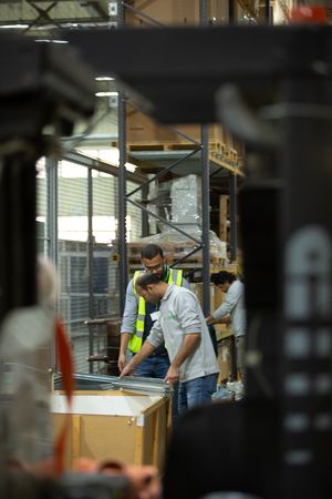 Workers examining materials on a workbench in a warehouse setting.