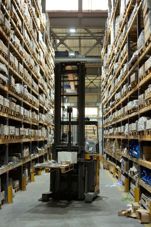 High warehouse shelving aisles with forklift and stacked inventory boxes.