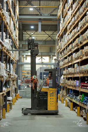 Forklift operator navigating between tall warehouse storage racks filled with inventory.