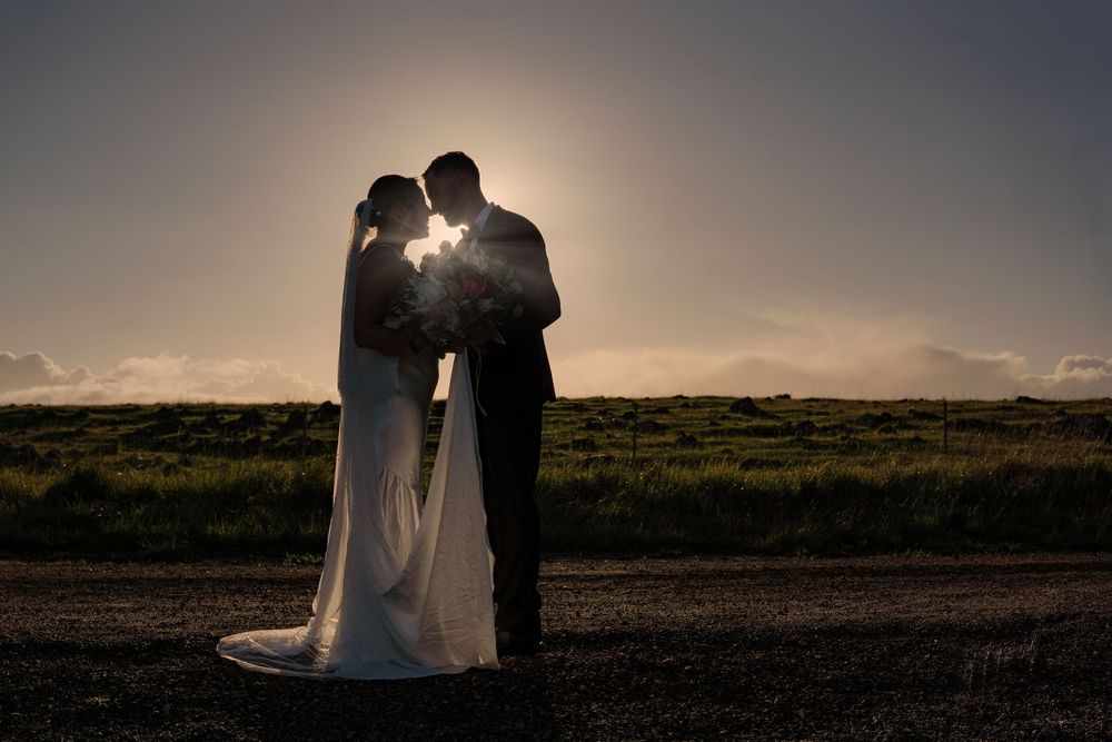 Silhouettes of a couple embrace during sunset in a grassy meadow with golden light creating a romantic atmosphere.