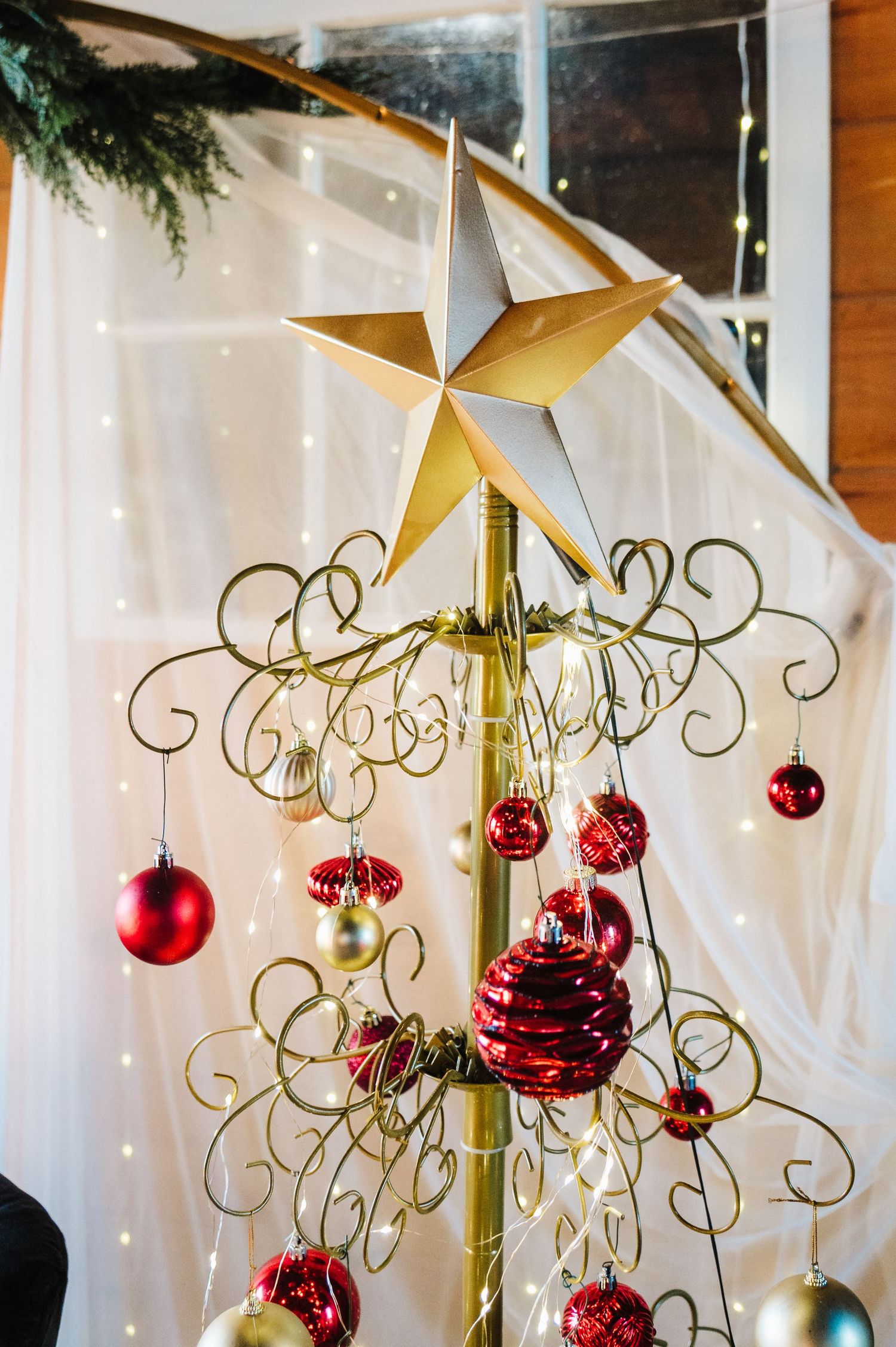 Gold metal Christmas tree with red and silver ornaments topped with a star, decorated with curling wire branches.