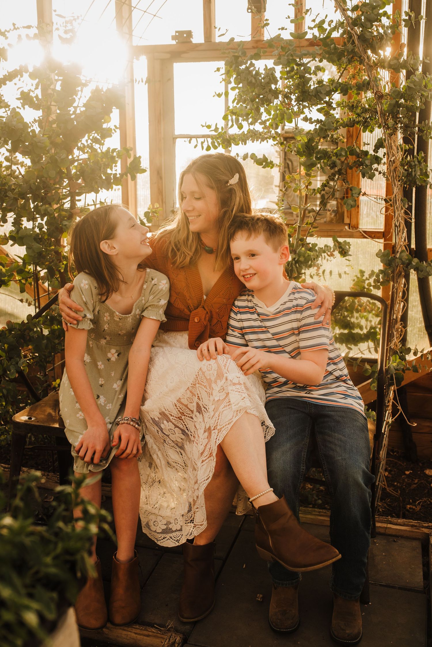 A mother and two children share a joyful moment on a swing inside a sunlit greenhouse.