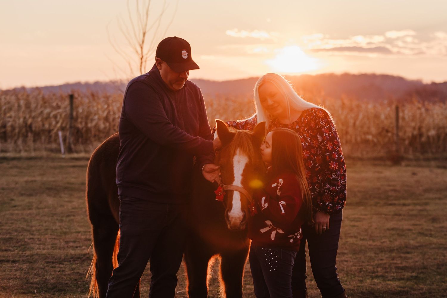 Couple petting a horse at golden sunset near a vineyard field in a warm outdoor setting.