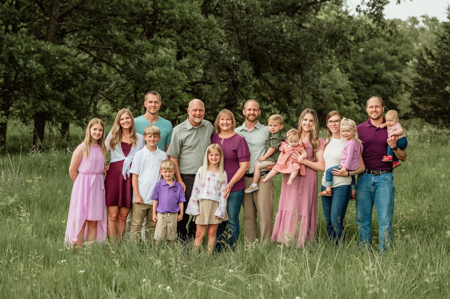 A group of people in summer attire stand together in a green outdoor field for a photo shoot.