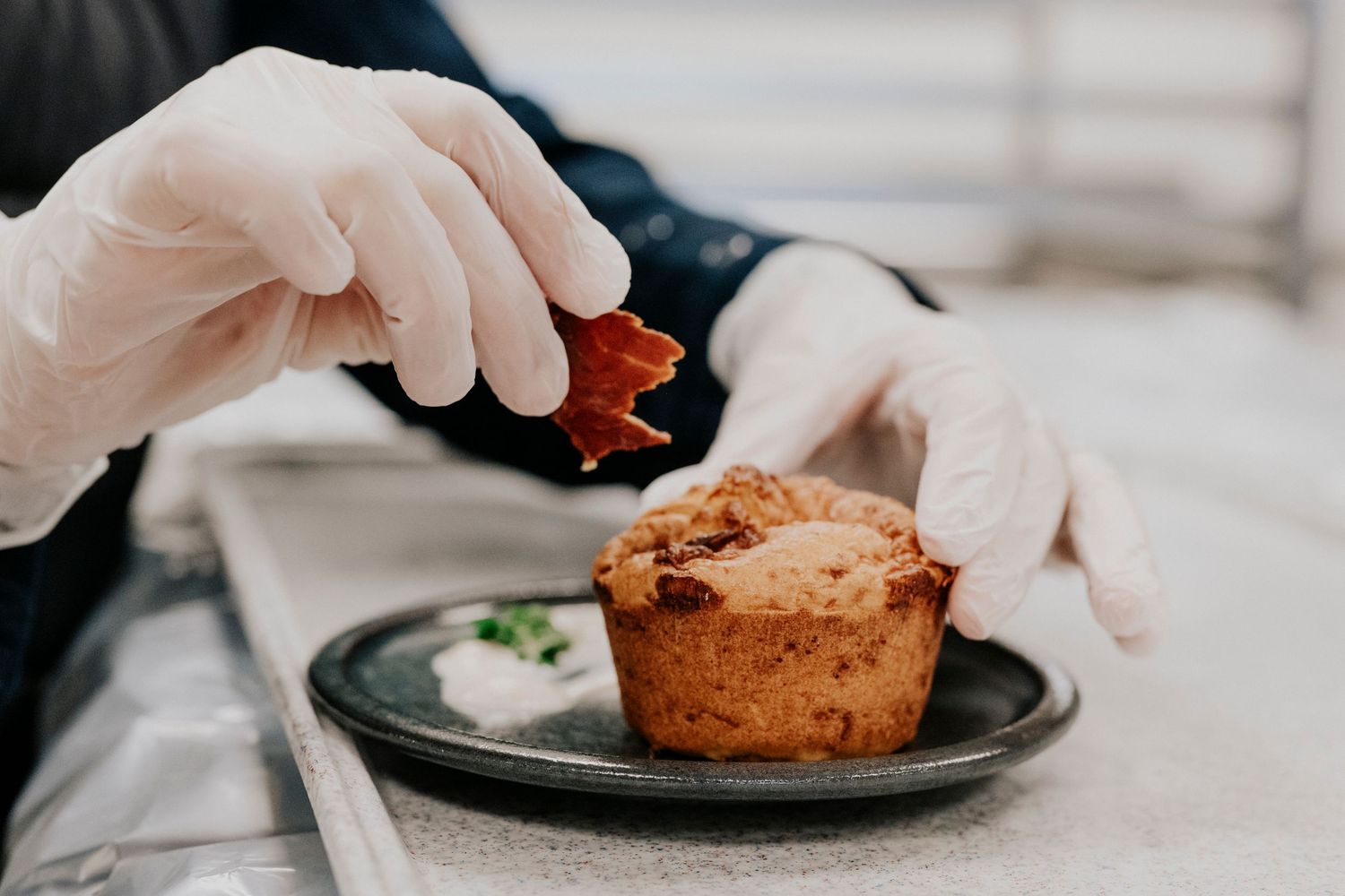 Photographe Toulouse: Gros plan des mains d'une personne garnissant soigneusement une création de dessert gastronomique à l'assiette.