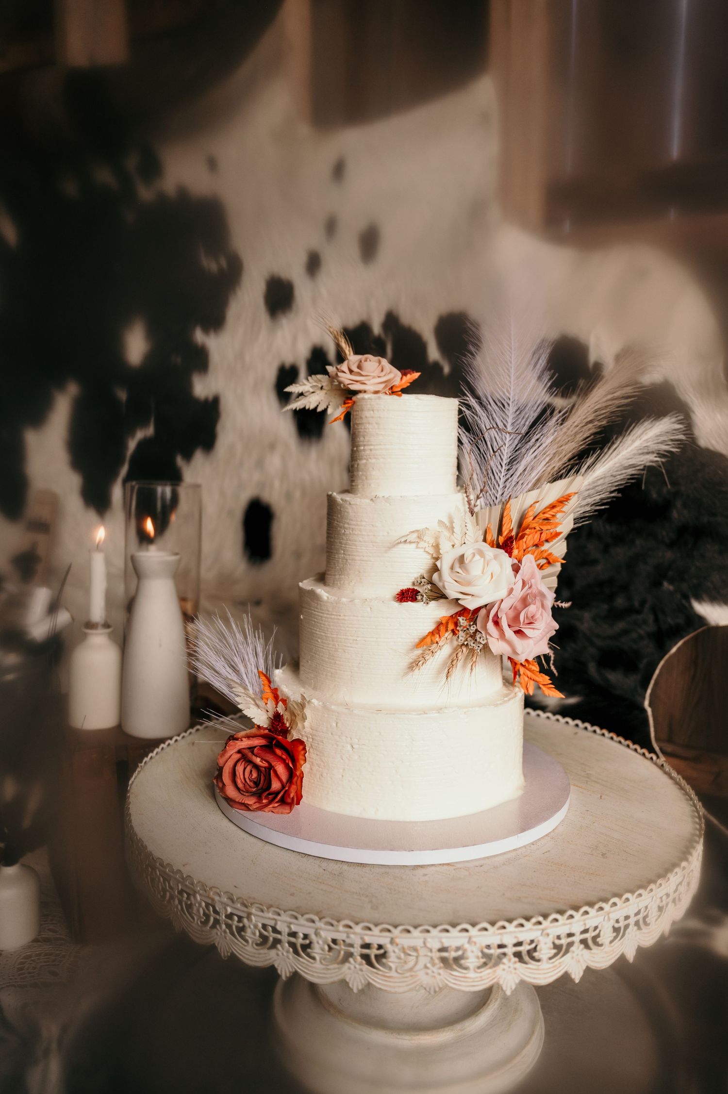 Elegant three-tier white wedding cake decorated with peach roses and feathers on a vintage lace cake stand.