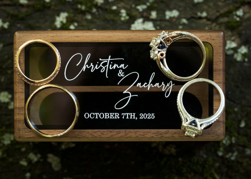 Wedding rings artistically photographed on dark wooden signs displaying wedding date details.