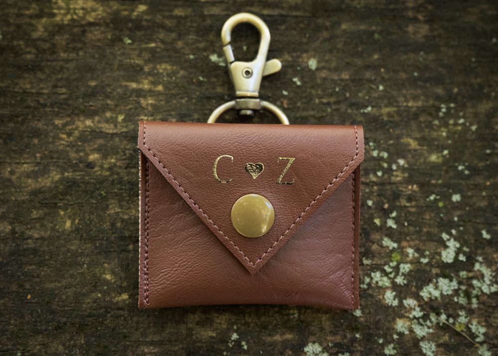 Collection of brown leather accessories and wedding rings arranged on weathered wood background.