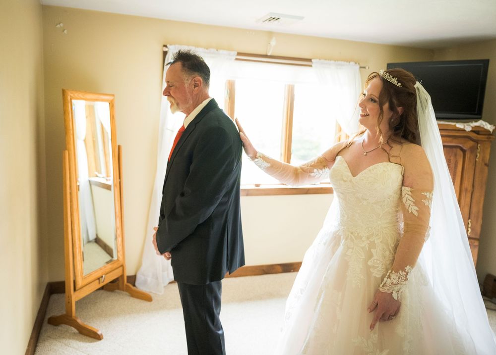 Wedding first look moment in a sunlit room with full-length mirror.