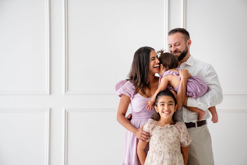 Family in coordinated purple and white outfits posing together against a white paneled wall.