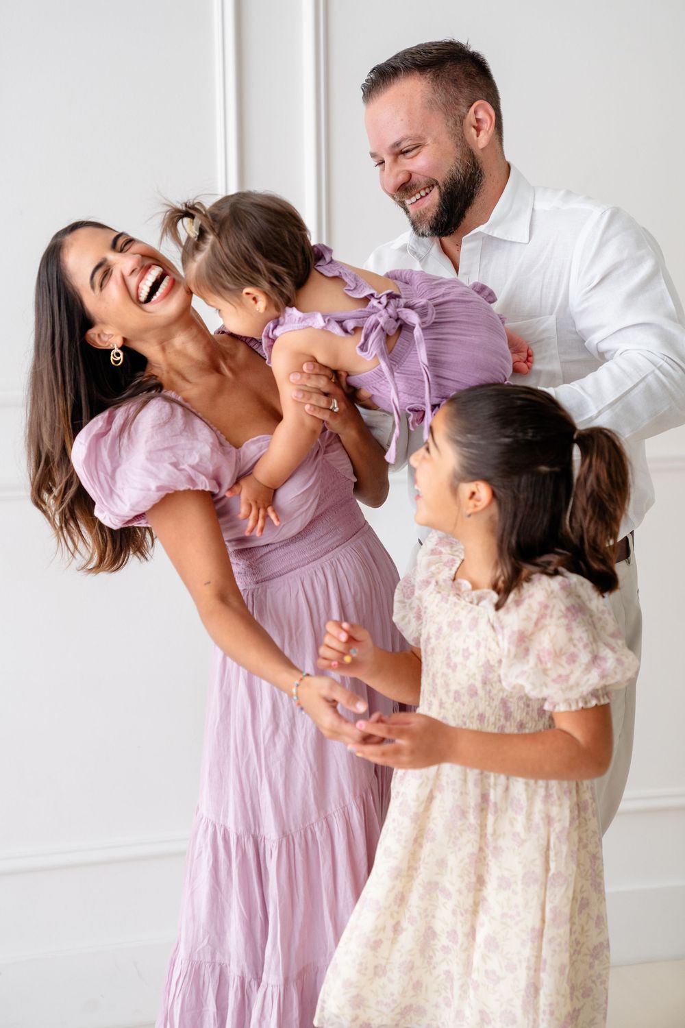 Candid family photoshoot showing joyful interaction and laughter in coordinated pastel outfits.