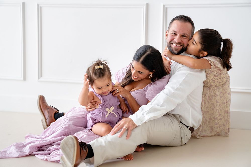 Family sits together on floor laughing and cuddling during casual photo session.