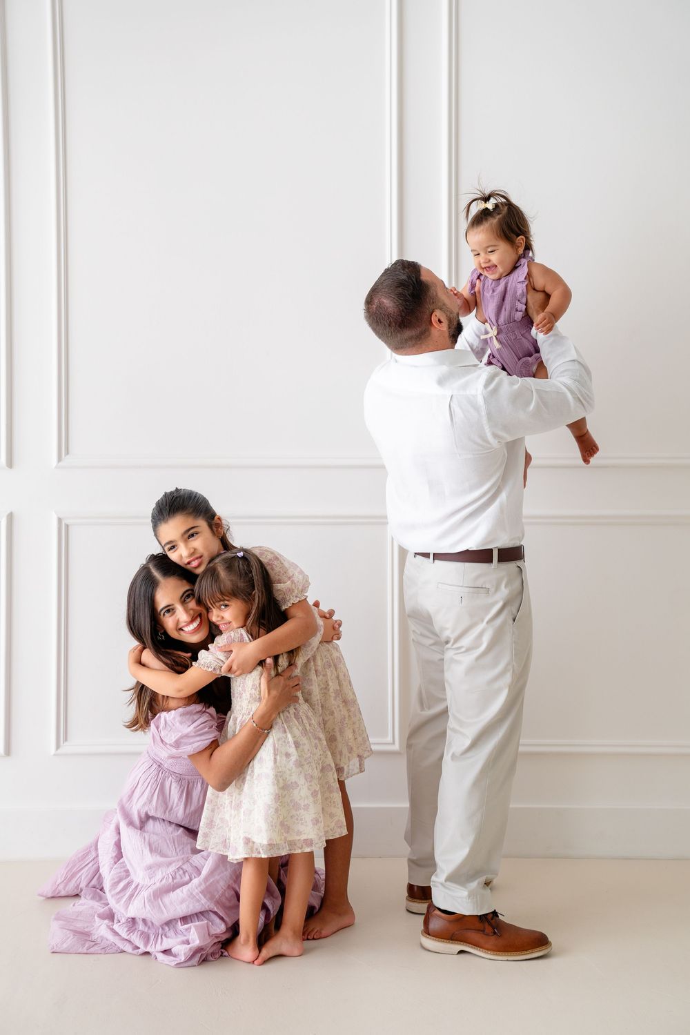 A playful series of interactions between loved ones wearing purple and white dresses against a bright white wall.