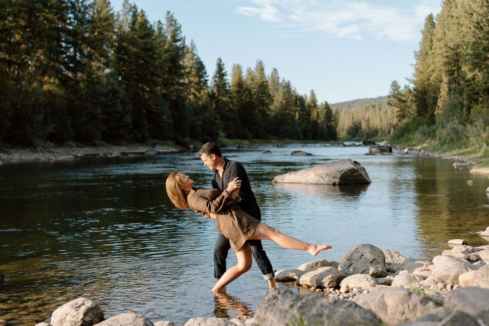 Playful moments captured at a riverside with pine trees and rocks creating a natural backdrop.