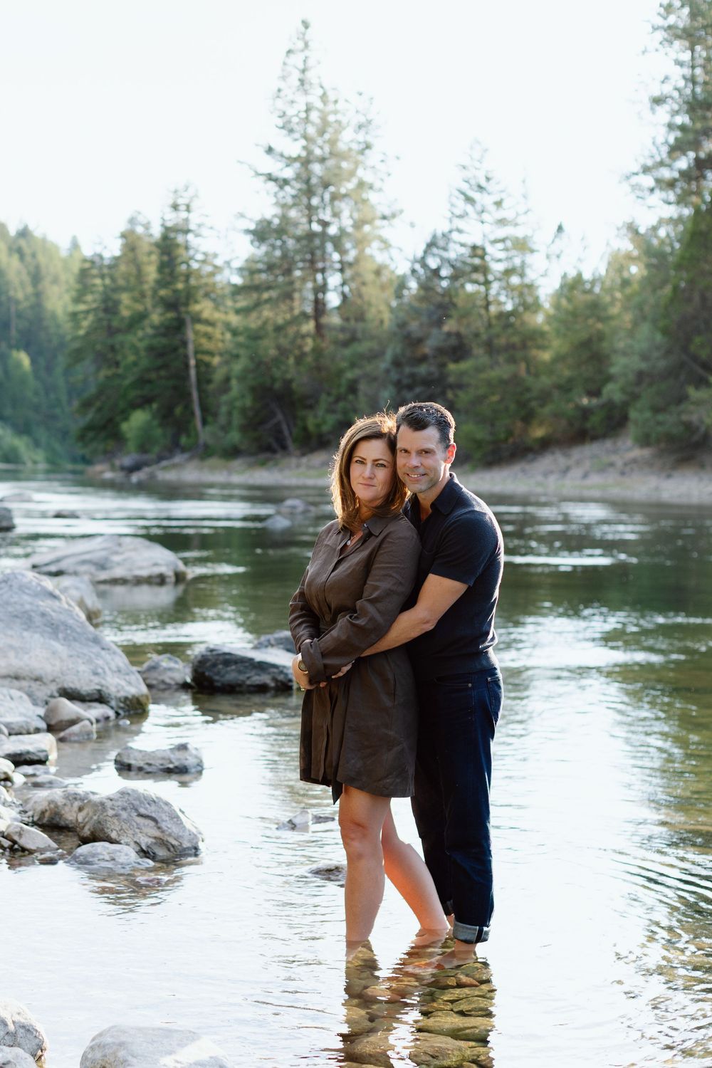 Intimate riverside photo session with pine forest backdrop and flowing water.