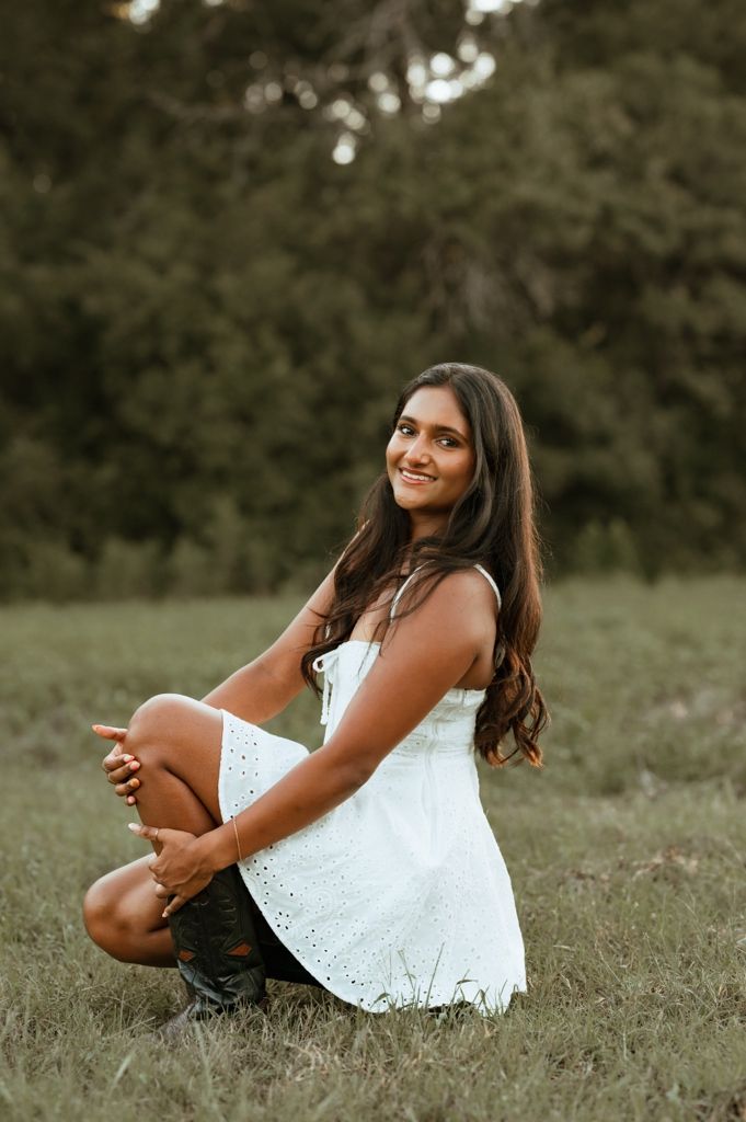 A summer portrait in a white eyelet dress sitting in a grassy field at golden hour.