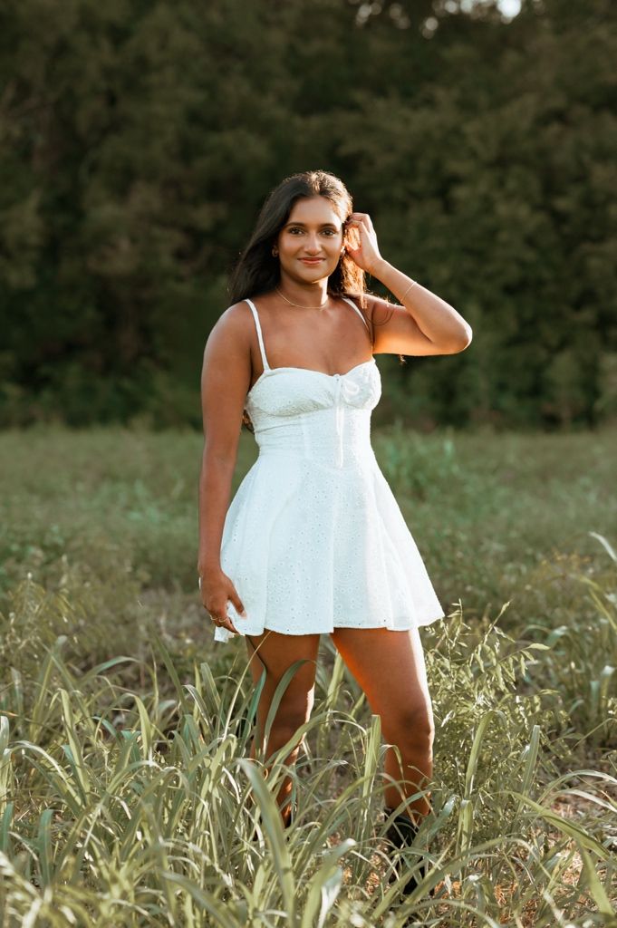 Woman in white sundress poses playfully in a grassy summer field during golden hour.