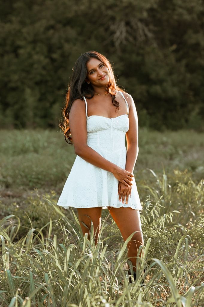 A woman in a white summer top poses gracefully in a sunlit field of tall grass.
