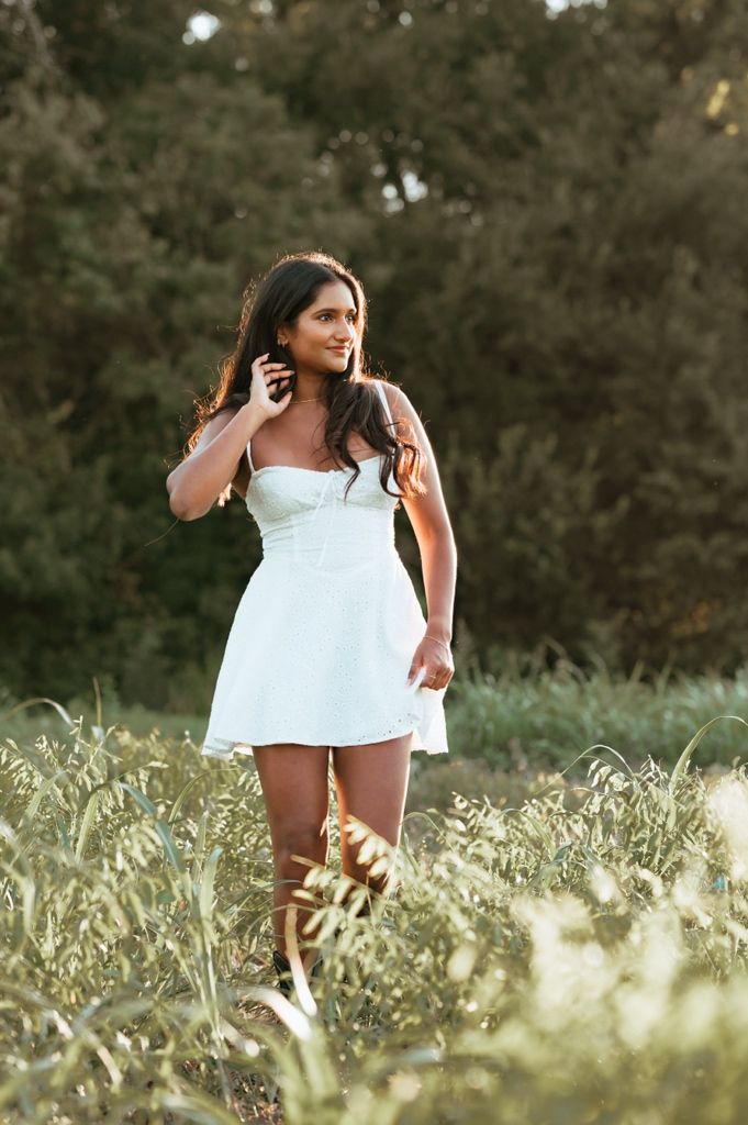 A person in a white dress poses gracefully in a sunlit field of tall grass during golden hour.