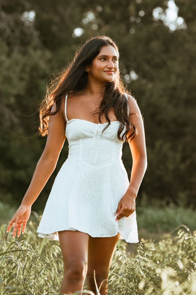 A person in a white sundress stands in a sunlit meadow during golden hour with windswept hair.