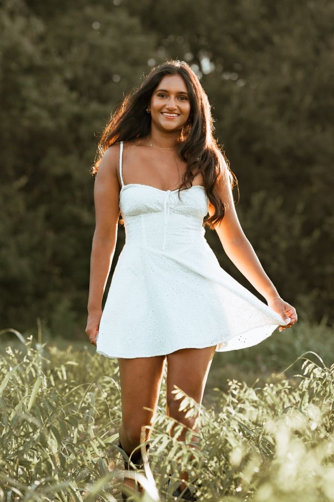 Person in a white summer dress poses gracefully in a sunlit meadow with wildflowers and natural lighting.