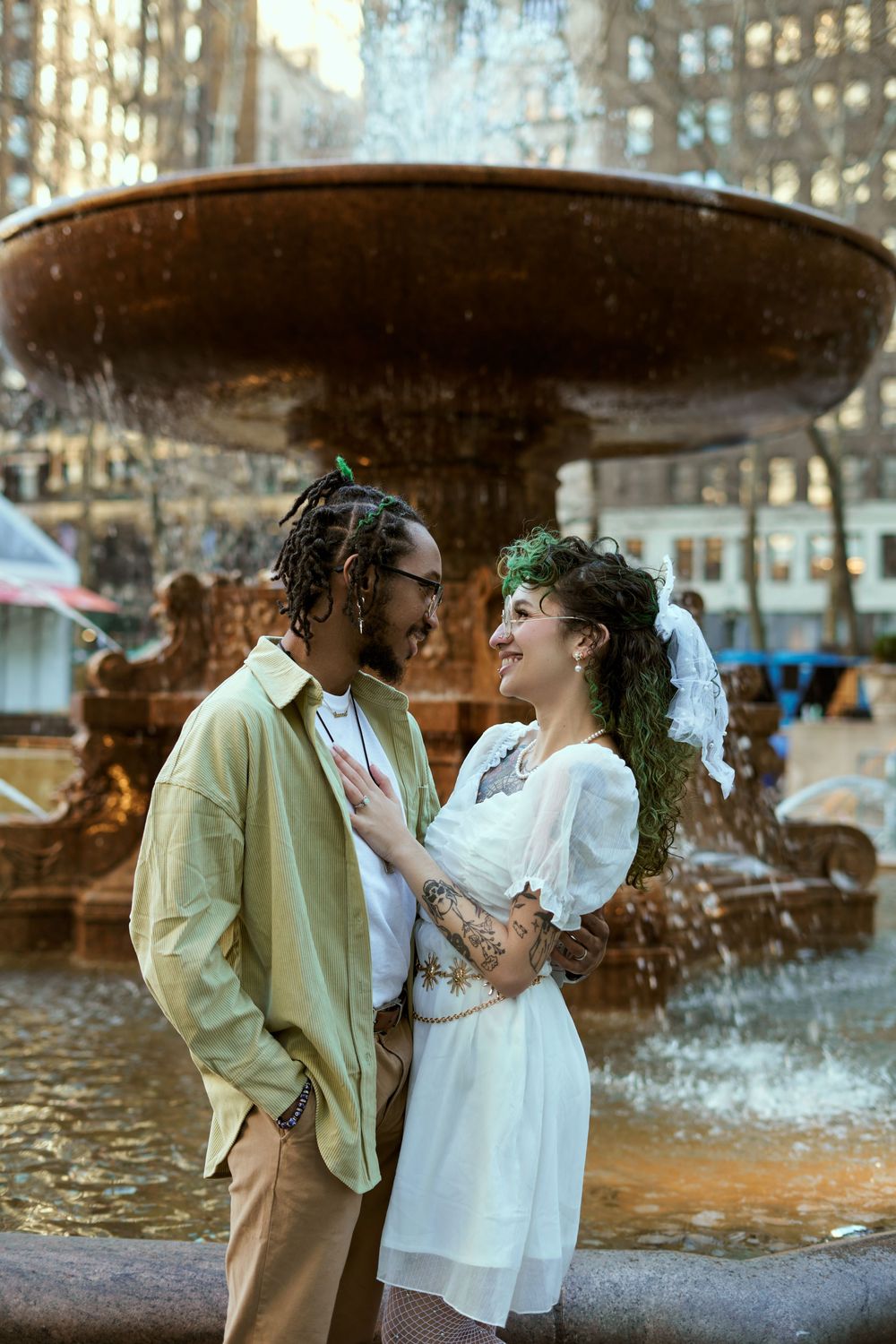Romantic couple shares tender moment in front of an ornate fountain with water spraying in an urban setting. Engagement shoot Manhattan