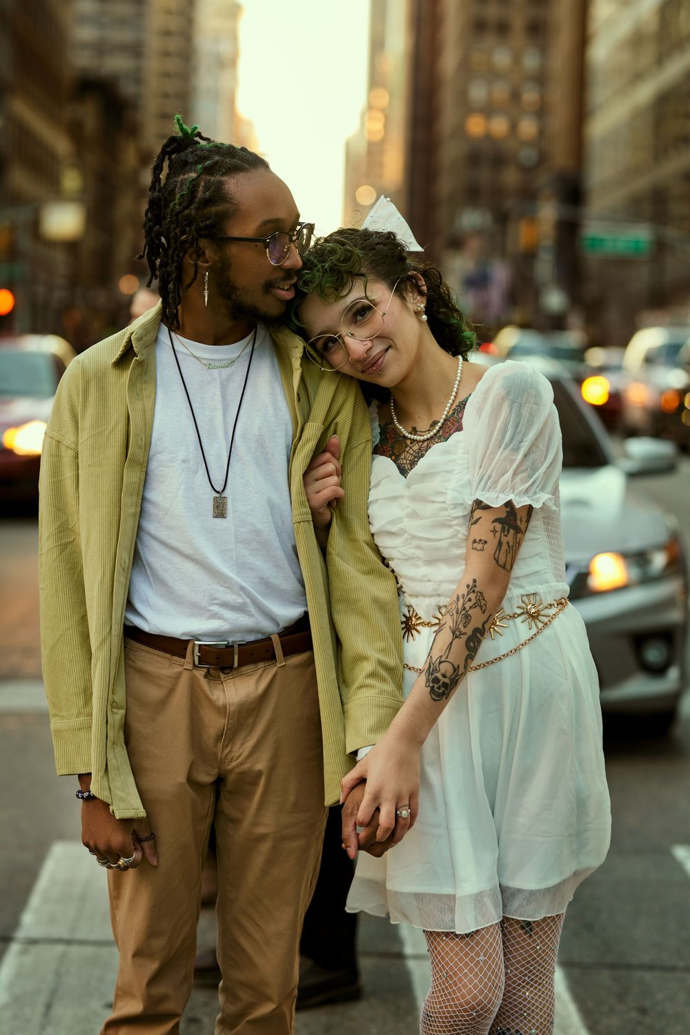 A stylish couple stands close together on a city street at dusk, wearing casual attire and sharing an affectionate moment. Engagement shoot