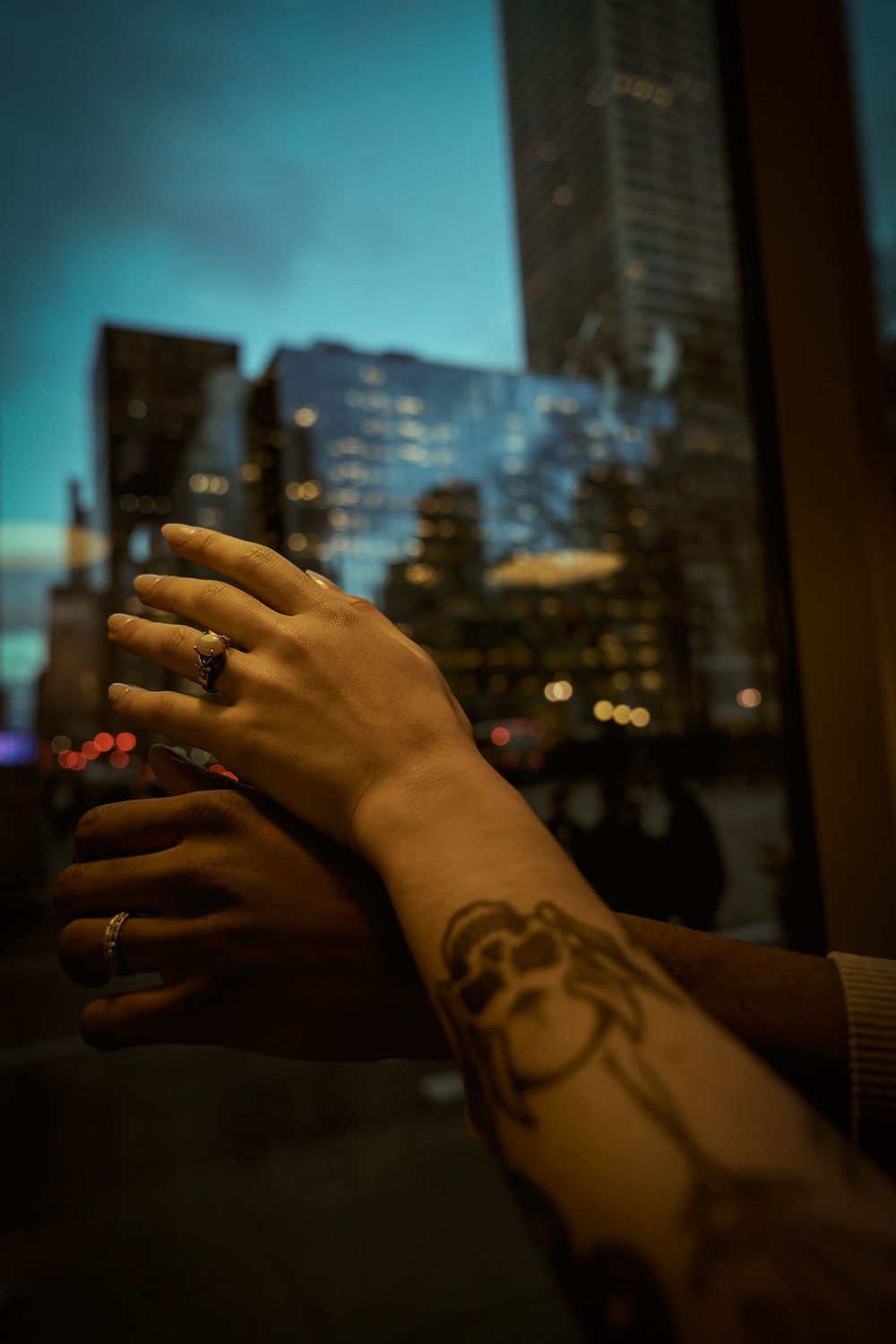 Tattooed arm rests against window with blurred city skyline and blue twilight sky in background. Engagement shoot Manhattan