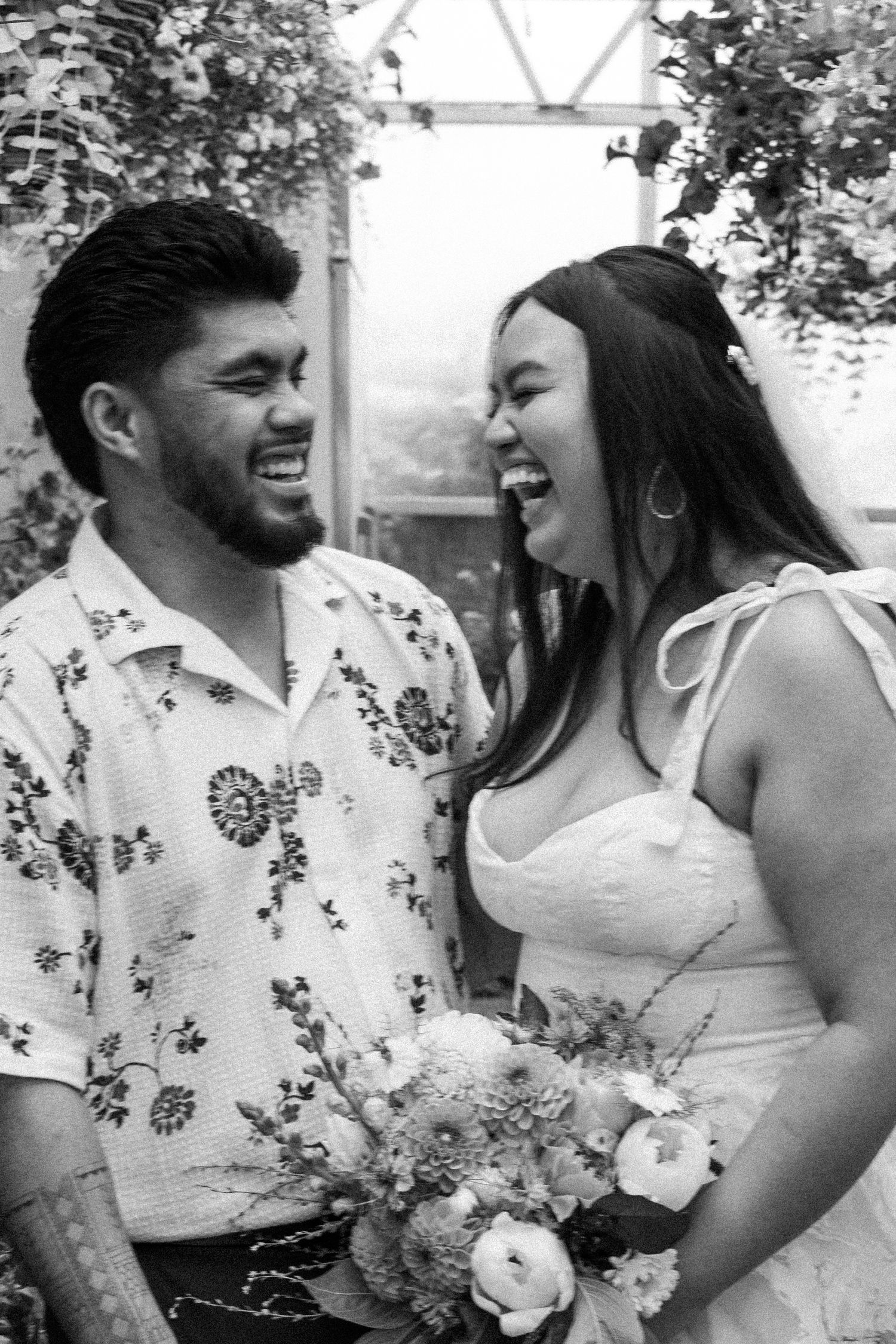 A laughing couple shares a joyful moment together at an outdoor venue, with the woman holding a bouquet in black and white.