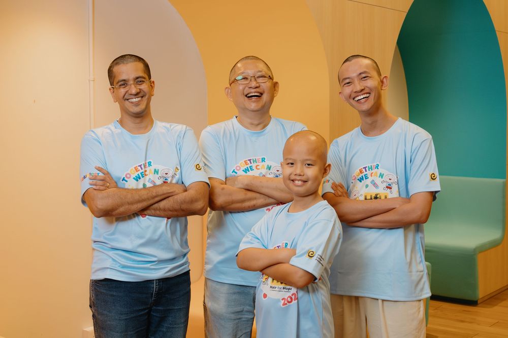 A group of volunteers wearing light blue t-shirts stand together and smile for a photo.